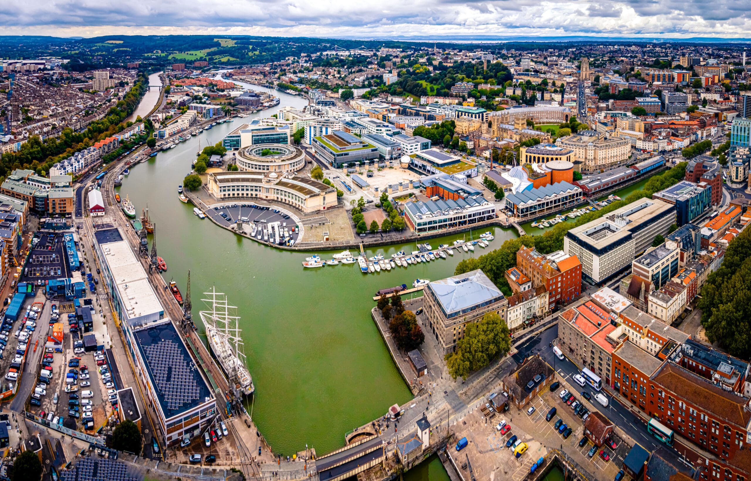 Aerial view of central Bristol, UK, showing the winding River Avon, modern buildings, historic architecture, a docked sailing ship, and green hills—an ideal backdrop for efficient House Clearance (+ 5 Variables See Questionnaire) services.